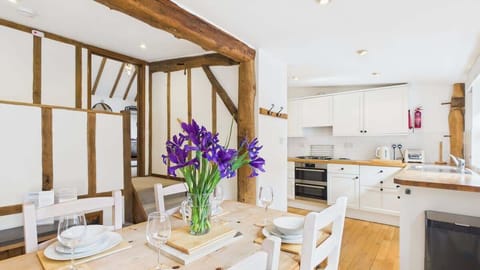 Open-plan living space at The Cote featuring sofas, Smart TV, farmhouse dining table and views into the kitchen, all in warm country style.
