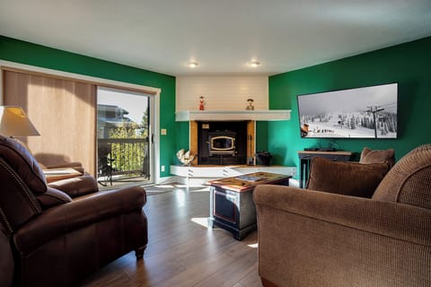 Unwind in your cozy living room with vibrant green walls, plush brown sofas, and a warm fireplace perfect for mountain evenings.