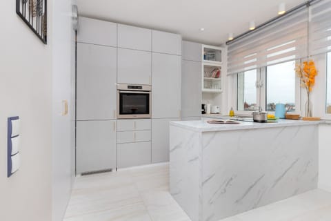 A sleek kitchen featuring a marble-topped island, white cabinetry, and modern appliances.