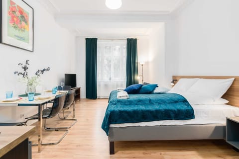 A bright studio apartment with a comfortable bed, turquoise bedding, and elegant decor.

