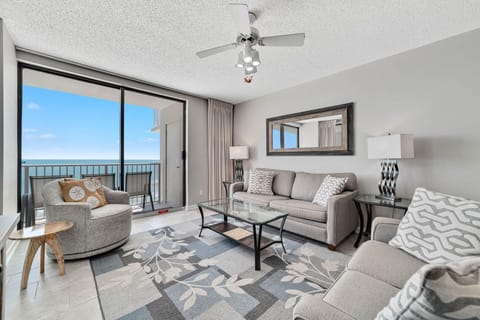 The generously accommodating living room is adorned with simple, classic decor, made more inviting by radiant natural light filtering through the glass doors from the balcony.