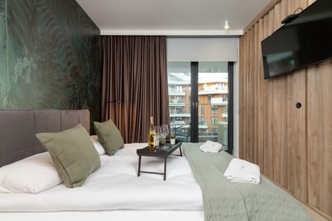 A stylish bedroom with a large bed, green bedding, and a wall-mounted TV, complemented by warm wooden accents.
