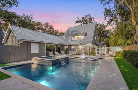 Modern coastal retreat featuring crystal-clear pool and spa under dramatic sunset skies, surrounded by lush tropical gardens.