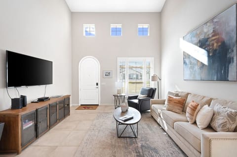 Bright living room w/ comfy seating, wall-mounted TV & natural light pouring in from tall windows