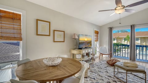 Open-concept living and dining area with round table, sofa seating, flat-screen TV, and balcony access