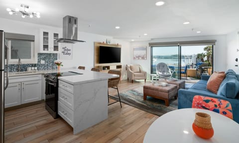 Bay Views- Living room with smart TV, comfortable couch and 2 lounge chairs. Kitchen with bar seating, 2-person dining table, and electric stove/range.