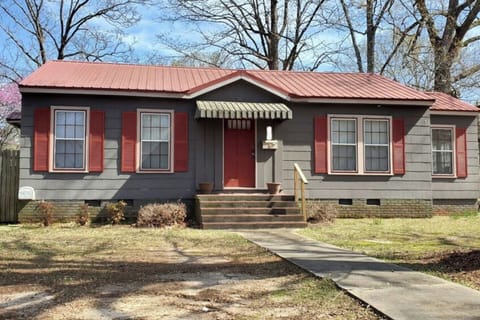 Charming single-story home with a classic red door, cozy front porch, and spacious yard shaded by mature trees.