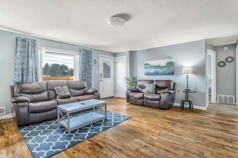 Reclining sofas arranged around a blue patterned rug create a relaxed living area for stretching out after a day away. Large windows bring in natural light while the coffee table keeps drinks, books, or a board game within easy reach.