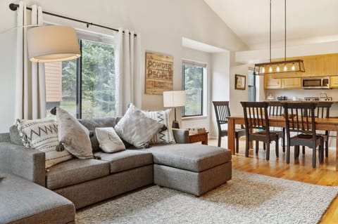 An open living and dining area on the main level is a gathering area full of natural light. The dining table seats 6 with four more at the bar. There is an oversized pullout couch and large TV in the living area, plus a console with games and books.