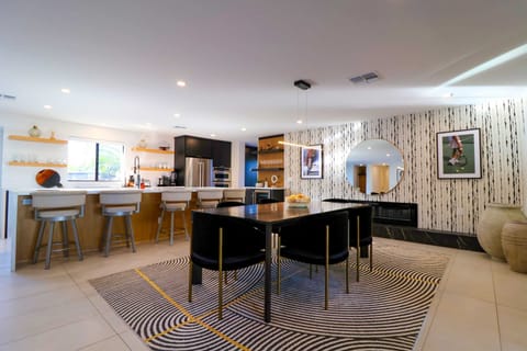 Luxe dining area with large dining table, adjacent digital modern fireplace and nearby kitchen bar seating for a seamless, stylish dining experience.