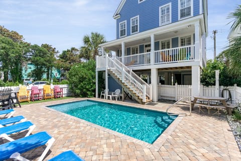 A charming blue coastal home with private pool surrounded by tropical palms and colorful outdoor seating areas.