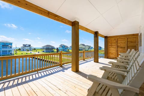 Spacious covered deck with rocking chairs overlooking waterfront views in Bolivar Peninsula vacation rental, perfect for relaxing outdoor seating and coastal breeze enjoyment.