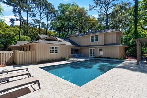 Sunny backyard escape with a modern two‑story home and a sparkling pool framed by tall trees.