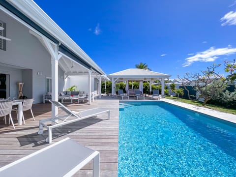 Oasis of relaxation: enchanting views from the pool, wooden deck and sun loungers, with a shaded patio in the background, complete with an elegant outdoor lounge.