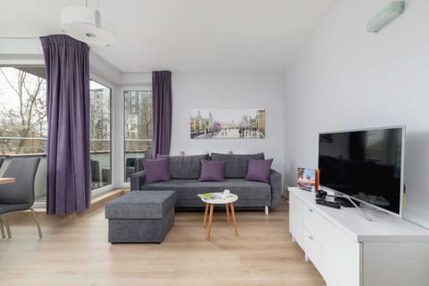 Elegant and stylish living room with an exit to the furnished balcony, television, comfortable double sofa bed and coffee table.