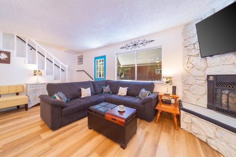 L-shaped dark gray sectional faces stone fireplace and wall-mounted TV beside blue entry door and window.