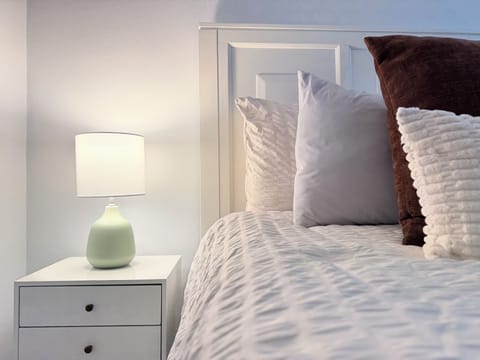 Cozy, light-filled bedroom with plush bedding and modern nightstand.