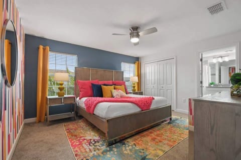 Bright and colorful bedroom featuring a plush queen bed with vibrant bedding, modern furniture, and fun decor. Natural light streams in through the windows, highlighting the unique wallpaper and cozy atmosphere. A perfect space to relax and recharge