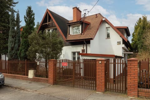 An exterior view of a charming house with a red brick facade and lush greenery surrounding it.
