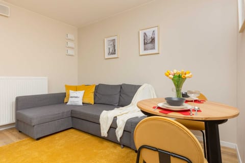 A cozy living area with a grey sectional sofa, yellow accents, and a round dining table with fresh flowers.
