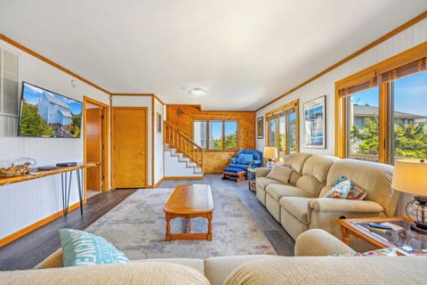 Settle into the sunlit living room where warm wood accents and plush seating invite you to relax. Large windows frame blue skies and greenery, filling your stay with natural light.