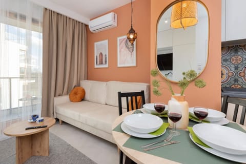 A cozy dining area with a round table, chairs, and decorative details. A large window allows natural light to brighten the warm-toned interior.