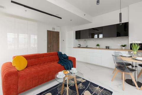 A modern living room with a bold orange sofa, complemented by cozy textiles. Large windows bring in ample natural light and provide a cityscape view.