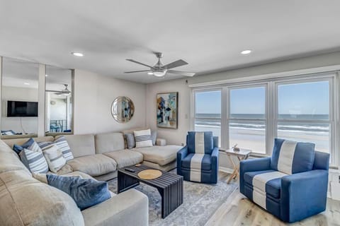 - Soak up panoramic beach views from this cozy, modern living room with plush seating & ocean toned accents
- Blue armchairs and a sectional make it perfect for lounging
- Large windows bring in natural light and endless coastal vibes
