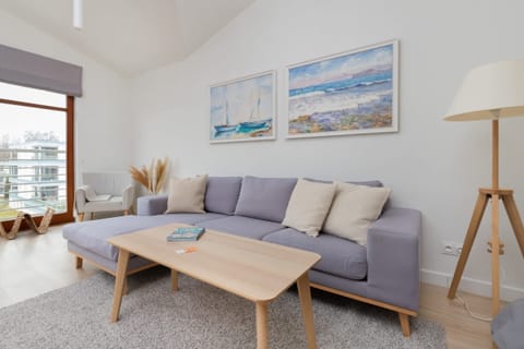 A bright living room featuring a comfortable sofa, light wooden furniture, and minimalist wall art.