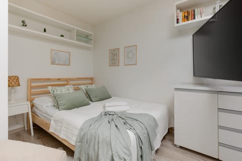 A cozy, multifunctional space combining a living room and a sleeping area. It features a comfortable beige armchair, a green blanket, and soft lighting for a relaxing atmosphere.