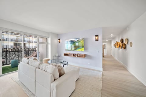 Living room with TV, sofa bed, and balcony - Step from your comfortable living area onto the lanai/balcony to enjoy Waikiki’s city energy and island breezes—an easy indoor-outdoor flow in the heart of Honolulu.