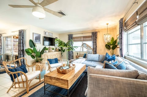 Boho living room with sofa, wood coffee table, woven accents, wall-mounted TV, tropical plants, and ceiling fan