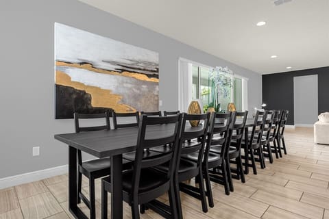 The dining area features a long, elegant table that seats 16, perfect for large gatherings. Above the table, a beautiful painting hangs on the wall, adding a touch of sophistication and charm to the space, creating a warm and inviting atmosphere.