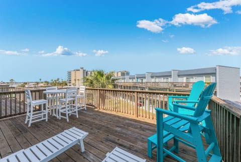 Expansive deck with colorful seating overlooking coastal buildings and palm trees under bright blue skies.