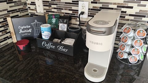 The image depicts a coffee bar with sugar packets, K-Cups, and a Keurig.