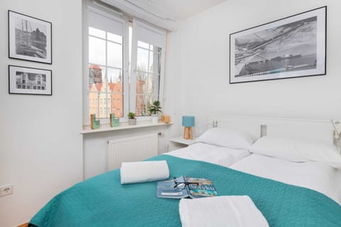 Bright bedroom with a cozy double bed, teal bedding, and large windows allowing natural light to fill the room.
