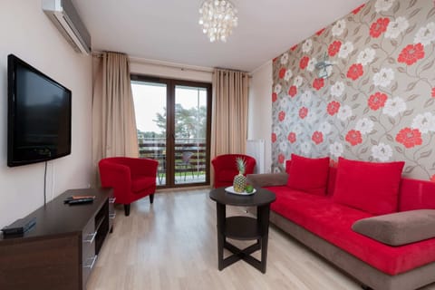 A cozy living room featuring a red armchair and a sofa, a wooden coffee table, and a TV mounted on the wall.
