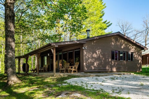 Brown wood siding and a covered porch with wooden rocking chairs overlook the shaded yard.
