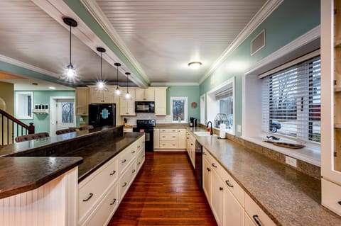 Kitchen with cream cabinets, speckled brown countertops, wood floors, and black appliances beneath paneled ceiling.