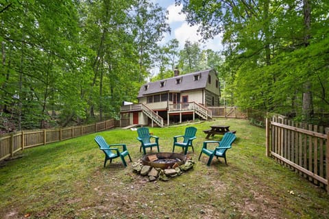 Fenced backyard with green Adirondack chairs encircling a stone-lined fire pit and a wooden picnic table nearby.