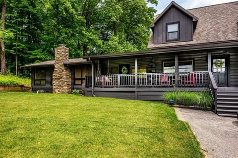 Dark wood siding and a stone chimney frame the cabin’s covered porch with red rocking chairs.