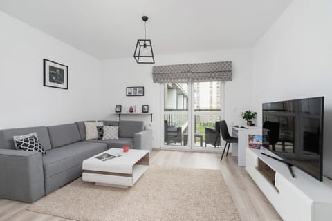 A modern living room featuring a gray sectional sofa, a white coffee table, and a TV mounted on a sleek entertainment unit. The decor is minimalistic with a black-and-white color scheme.
