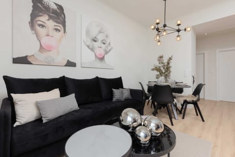 A stylish and modern living room with a black sofa, decorative pillows, and artistic wall decor featuring portraits, creating an elegant ambiance.