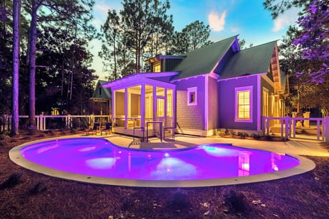 Modern vacation home nestled among towering pines features stunning purple LED lighting and curved pool creating magical evening ambiance.