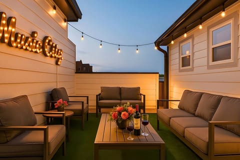 Rooftop terrace at dusk with outdoor sofas, string lights, wine bottle, and lush greenery