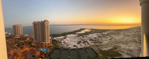 Stunning sunset view showcasing nearby high-rise buildings, coastal waters, tennis courts, and natural shoreline visible from the property's elevated vantage point.