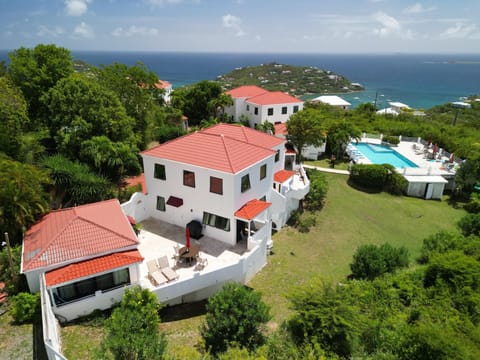 Aerial view of white stucco villa with red tile roofs, spacious patio, pool, and ocean backdrop.