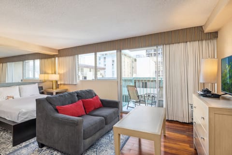 Your spacious suite features plush bedding, a cozy lounge area with sofa, and a private balcony where you can enjoy views of the surrounding cityscape. Rich wood flooring and soft lighting create a warm, inviting ambiance.
