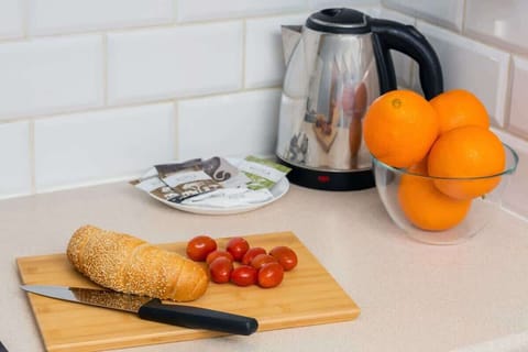 A kitchen countertop with a coffee station, fresh oranges, bread, and tomatoes, offering a warm and welcoming vibe.
