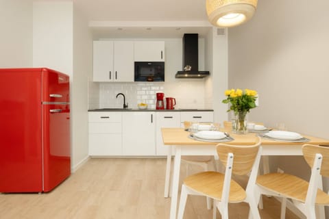 A modern kitchen and dining area featuring a red fridge, white cabinetry, and a wooden dining table set for a meal.
